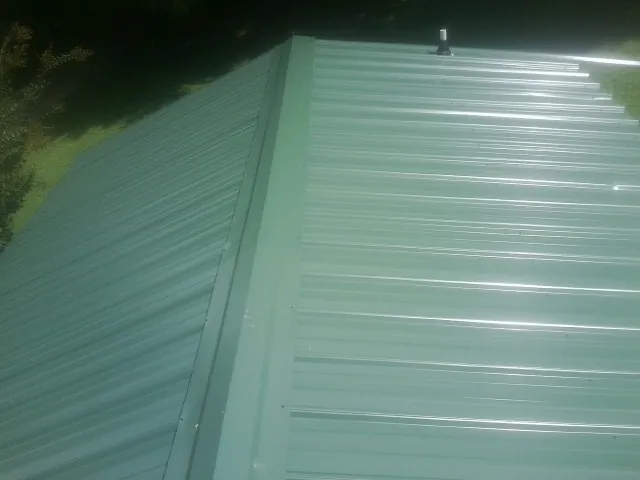 New green metal panels meeting at the ridge of a roof — Flat Roof Repair work by our crew in Frankfort