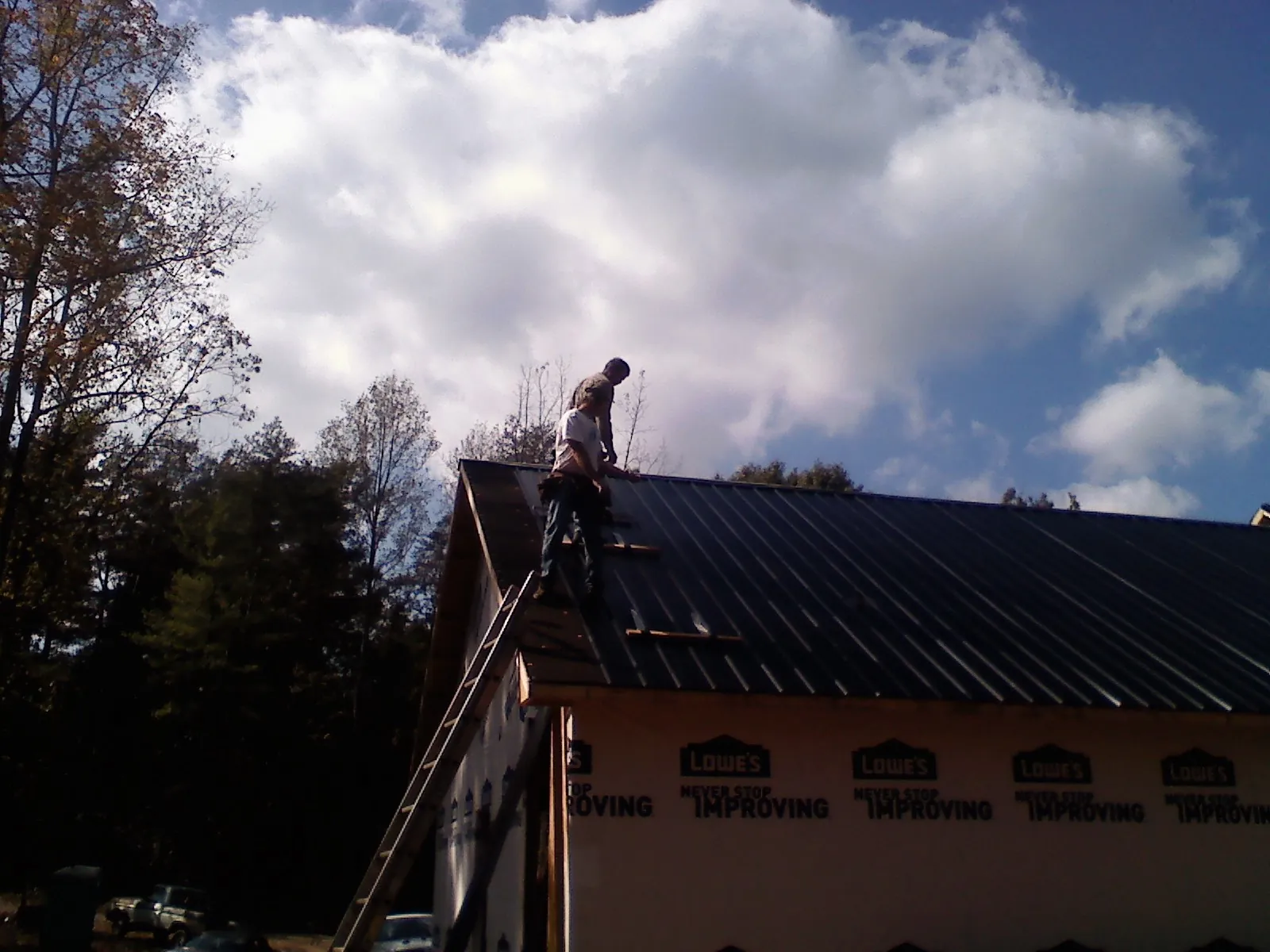 Roofer fastening dark metal panels high against a cloudy sky, from a Roof Inspection job in Frankfort